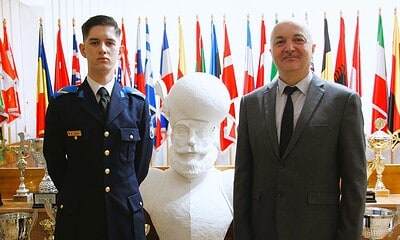 Elev în uniformă militară și profesor lângă statuia lui Luca Perța, la etapa națională a Olimpiadei.