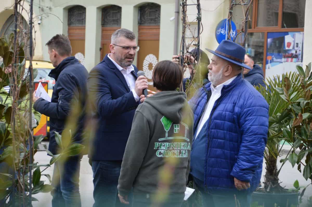 Trei persoane discutând la Plant Fest 2026 cu flori și arbuști în fundal.