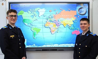 Elevi în uniformă militară în fața unui glob pământesc digital.