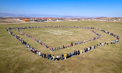 O mulțime de oameni formează un cerc în formă de inimă pe un teren deschis, simbolizând comunitatea.