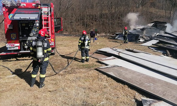 Echipaj de pompieri stingând focul la o construcție afectată de incendiu.