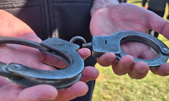 Cătușe metalice ținute în mâini, simbol al arestării sau al justiției.