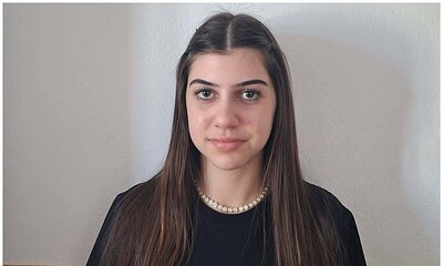 Fată tânără cu păr lung, ochi căprui și zâmbet subtil, portret în interior.