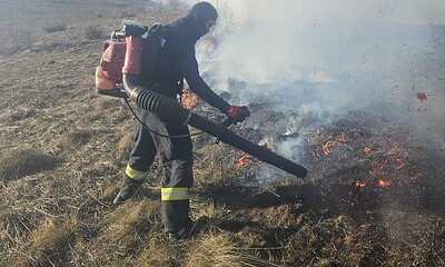 Pompier stingând un incendiu de vegetație în Râmeț, cu elicopterul SMURD solicitat pentru intervenți.