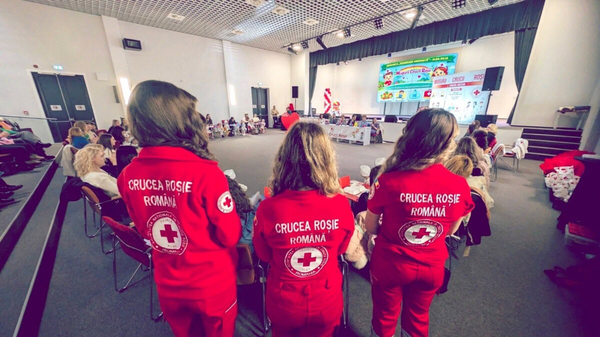 Trei copii de grădiniță în uniforme Roșia Crucii România participând la activități de prim ajutor.